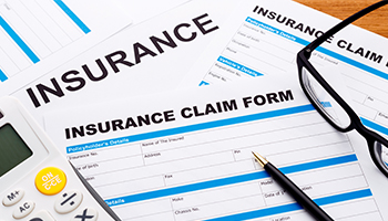 Insurance claim form with a pen, eyeglasses, and calculator on a desk